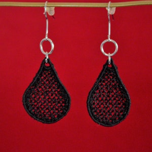 May include: A pair of black teardrop-shaped earrings with a delicate lace design. The earrings are made of metal and have a silver hook closure.
