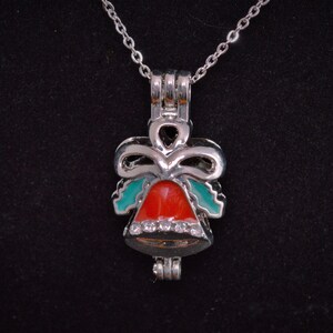 May include: A silver charm necklace featuring a red and green bell charm. The bell has a bow and holly leaves. The charm is decorated with small clear rhinestones.