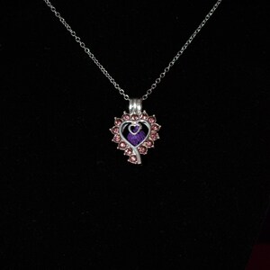 May include: A silver necklace with a heart-shaped pendant. The pendant is decorated with pink rhinestones and has a smaller heart inside. The smaller heart is purple.