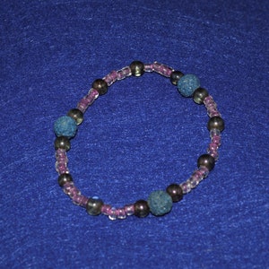 May include: A bracelet made with small, clear beads and larger, dark blue beads. The bracelet is on a blue background.