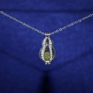 May include: A silver necklace with a cage pendant featuring a green stone inside. The necklace is on a blue background.