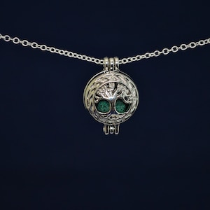 May include: A silver chain necklace with a round pendant featuring a tree of life design. The pendant is open and has a green stone inside.
