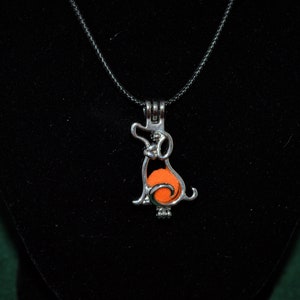 May include: A silver charm necklace with a dog-shaped pendant. The pendant contains an orange glass orb.