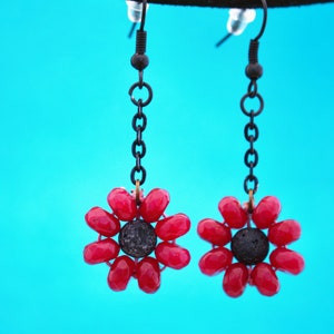 Puede incluir: Un par de pendientes colgantes con abalorios en forma de flor roja y centros de roca de lava negra.