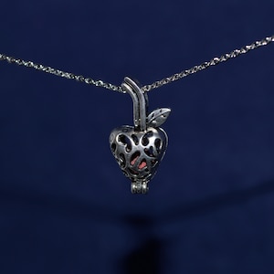 May include: A silver chain necklace with a heart-shaped pendant. The pendant is open and has a delicate design. The heart is filled with a small, pink stone.
