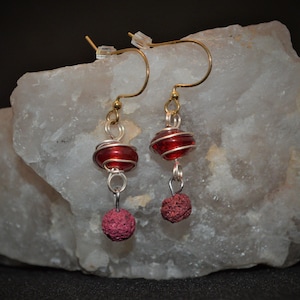 Könnte beinhalten: Rote Glas- und Lavastein-Ohrringe mit goldenen und silbernen Draht-Akzenten.