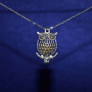May include: A silver owl-shaped pendant necklace with a detailed design. The pendant is hanging from a silver chain against a blue background.