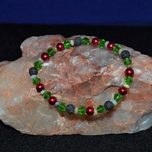 May include: A bracelet made with red, green, and black beads. The bracelet is on a light brown rock.