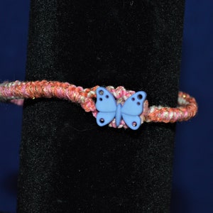 May include: A pink and gold braided bracelet with a blue butterfly charm.