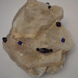 Puede incluir: Un collar delicado con una cuerda transparente y cuentas de color azul oscuro y negro.