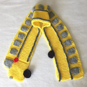 May include: Yellow knitted scarf shaped like a school bus with gray windows and black wheels.