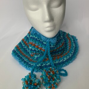 Peut inclure: Un chauffe-cou crocheté rayé bleu et orange avec deux pompons.