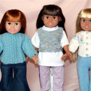 May include: Three dolls wearing knitted sweaters and trousers. The doll on the left is wearing a blue sweater and blue jeans. The doll in the middle is wearing a white shirt with a multi-coloured knitted waistcoat and lavender trousers. The doll on the right is wearing a white sweater with a light blue and pink pattern and light blue jeans.