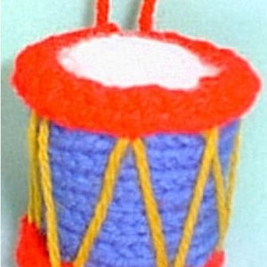 May include: A small, red and blue knitted drum with yellow yarn accents. The drum has a white top and is attached to a red string.