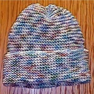 May include: A knitted hat with a multi-colored pattern in shades of blue, green, pink, and white. The hat has a folded brim.