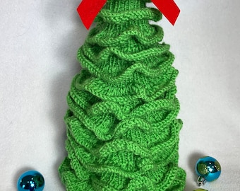 Könnte beinhalten: Ein grüner gestrickter Weihnachtsbaum mit einer roten Samtschleife oben. Der Baum ist von bunten Ornamenten umgeben.