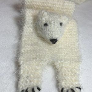 May include: White knitted scarf with a polar bear face and black claws. The scarf is made of a fluffy yarn.