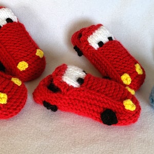 Könnte beinhalten: Vier Paar gestrickte Babyschuhe in Form von Autos. Zwei Paare sind rot mit gelben Akzenten und zwei Paare sind blau mit weißen Akzenten.