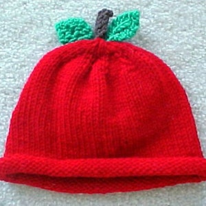 May include: A red knitted hat shaped like an apple with green felt leaves on top.
