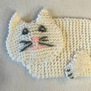 Peut inclure: Chat en tricot blanc avec un nez rose et des moustaches grises. Le chat est couché, ses pattes sont visibles.