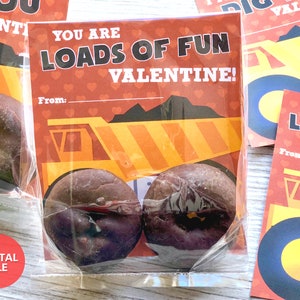 May include: A Valentine's Day card with a yellow dump truck and the text "You are loads of fun Valentine!"  The card is in a clear plastic bag with two chocolate donuts.