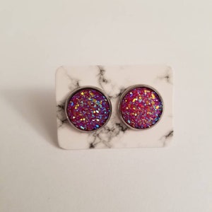 May include: A pair of silver stud earrings with pink and purple glitter embedded in the round face.