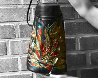 May include: Black leather handbag with a long strap and a colorful floral design. The design features gold, red, and teal colors.