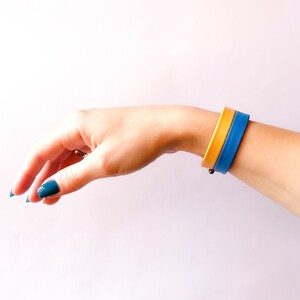 May include: A blue and yellow bracelet on a person's wrist. The bracelet is made of two bands of leather, one blue and one yellow.