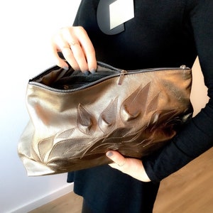 May include: A gold leather clutch with a floral design. The clutch has a zipper closure and is made of a soft, supple leather.