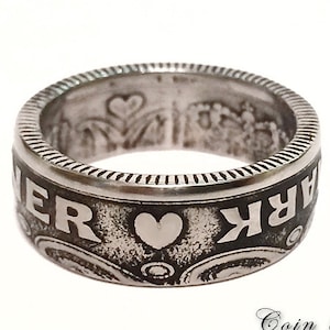 May include: Silver ring made from a repurposed coin. The ring features the words "remarkable" and a heart design.