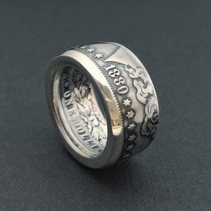 May include: A silver ring crafted from a coin, featuring the year 1880 and intricate details. The ring showcases a detailed design with stars and floral patterns, offering a unique and vintage aesthetic. The ring is a statement piece.