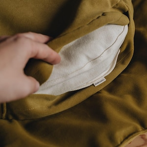 Pu&ograve; includere: Un cuscino in tessuto giallo senape con una fodera in cotone bianco. La fodera ha un'etichetta piccola che recita "band & roll."