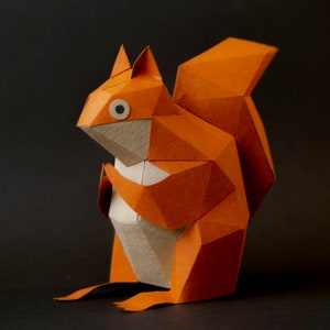 May include: Orange papercraft squirrel with a geometric design. The squirrel is standing on a black surface.