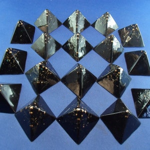May include: A set of 16 black pyramid-shaped objects with gold accents. The pyramids are arranged in a grid pattern on a blue surface.