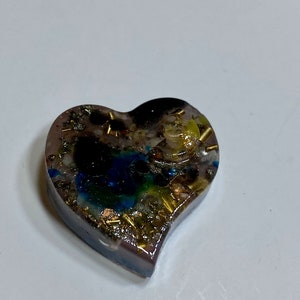 May include: A heart-shaped resin ornament with embedded crystals and gold flakes. The resin is clear and allows the crystals to be seen. The ornament is a light purple color.