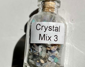 May include: A small glass bottle with a cork stopper filled with a variety of small crystals. The bottle has a white label that reads "Crystal Mix 3".