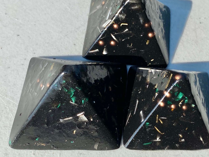 May include: Three black pyramid-shaped objects with gold and green glitter embedded in the resin. The pyramids are stacked on top of each other.
