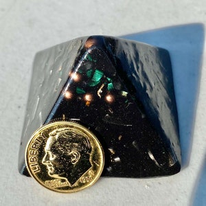May include: A black pyramid-shaped object with green and gold flecks. A gold-colored US dime coin with the year 1990 is in front of the pyramid.