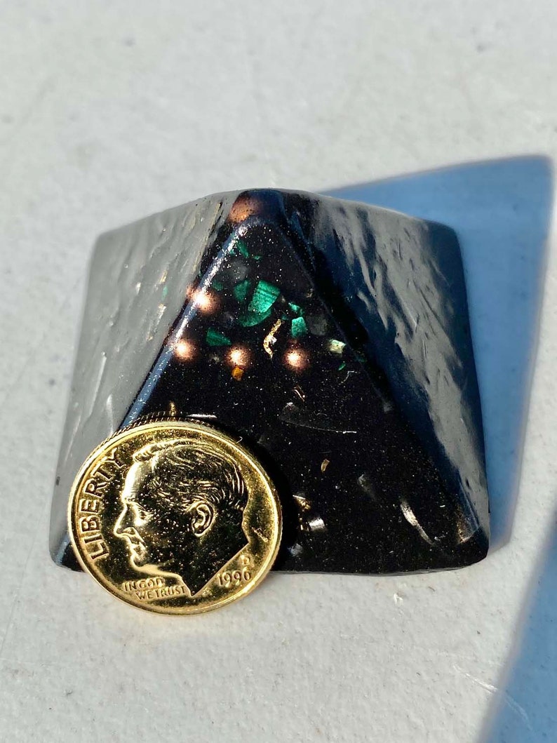 May include: A black pyramid-shaped object with green and gold flecks. A gold-colored US dime coin with the year 1990 is in front of the pyramid.