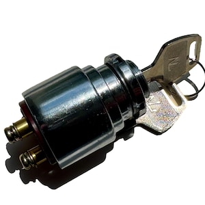 May include: A shiny, chrome-finished ignition switch with a key inserted. The key has a ring and the letters "NL" are visible. The switch has two terminals with springs. The item is isolated on a white background.