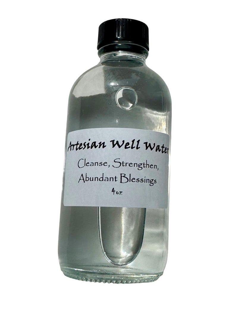 May include: A clear glass bottle with a black cap, filled with liquid. A white label on the bottle reads "Artesian Well Water" with the words "Cleanse, Strengthen, Abundant Blessings" and "4 oz".