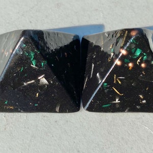 May include: Two black pyramid-shaped objects with gold and green flecks embedded in the resin.