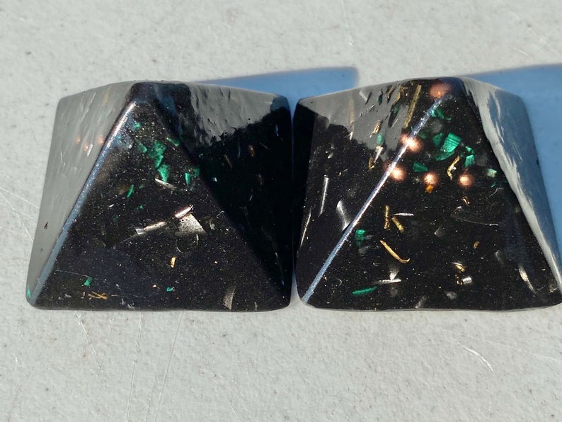 May include: Two black pyramid-shaped objects with gold and green flecks embedded in the resin.