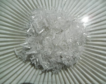 May include: A close-up of a pile of white, needle-like crystals on a white, textured surface.
