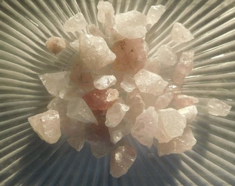May include: A collection of pink and clear quartz crystals in various sizes and shapes. The crystals are arranged on a white, textured surface.