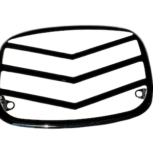 May include: A black, chrome-finished motorcycle headlight grill with a curved rectangular shape. The grill features a series of horizontal and chevron-shaped bars, and mounting holes on the bottom corners. The design is sleek and modern.