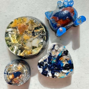 May include: Four resin ornaments with different designs. One is a round ornament with gold and white flecks, another is a round ornament with blue and gold flecks, another is a heart-shaped ornament with blue and white swirls, and the last is a blue and red ornament shaped like a cartoon animal.