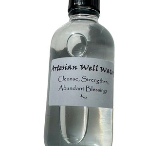 May include: A clear glass bottle filled with liquid, featuring a black cap and a white label. The label reads "Artesian Well Water" with the phrases "Cleanse, Strengthen, Abundant Blessings" and "4 oz."