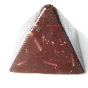 May include: A dark brown chocolate pyramid with a textured surface and flecks of green and gold.