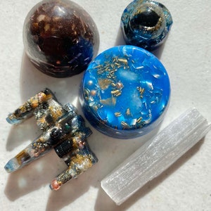 May include: A set of five crystal healing objects, including a blue and gold resin orb, a white selenite wand, a brown and gold resin orb, a blue and gold resin orb, and a blue and gold resin spaceship.
